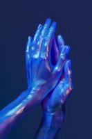 Human hands painted in metallic blue and purple paint with holographic effect against dark background, creating surreal artistic composition.
