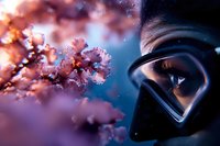 Close-up view of protective face mask and glasses against blooming pink cherry blossoms with soft bokeh effect and dramatic blue evening sky background.