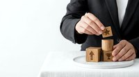 Professional businessman in dark suit stacking wooden blocks with energy symbols on white desk, representing sustainable business growth and renewable power.