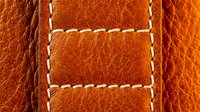 Orange leather texture with white decorative stitching seams creating geometric pattern for luxury fashion accessories and upholstery design projects.