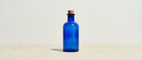 Cobalt blue glass bottle with cork stopper isolated on sandy beige background, ready for product design, cosmetics, potion, or apothecary branding.