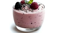 Fresh berry smoothie in glass bowl topped with blackberry, raspberry and mint leaf garnish on white background, creamy pink texture with dark specks.