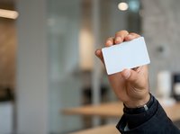 Man holding blank white business card in modern office environment for corporate branding and professional networking purposes.