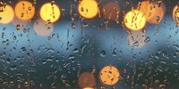 Raindrops on window glass with blurred golden bokeh lights creating atmospheric mood during evening rainfall, water droplets reflecting city illumination.