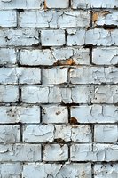 Old brick wall with peeling white paint showing weathered texture and decay. Rough surface with cracks and exposed areas creates industrial grunge background.