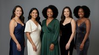 Five diverse women in elegant evening dresses posing together against gray background, representing friendship, celebration and formal fashion styles.