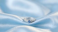 Sapphire and diamond engagement ring resting on soft blue silk fabric, showcasing luxury jewelry design for wedding and bridal collections.