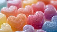 Colorful heart shaped gummy candies in rainbow colors with sugar coating, macro close up view showing texture and sparkle. Sweet treats arranged in rows.