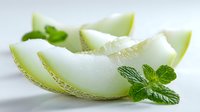 Fresh honeydew melon slices with mint leaves on white background, showcasing juicy texture and vibrant green rind for food photography and culinary design.