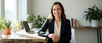 Professional businesswoman smiling confidently at modern office desk with laptop and plants creating productive workspace atmosphere for corporate success.