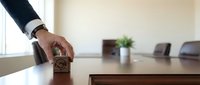 Business professional hand placing wooden approval stamp on conference table in modern office meeting room for document authorization and corporate decisions.