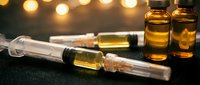 Medical syringe with amber vials on dark surface with warm bokeh lights creating pharmaceutical laboratory atmosphere for healthcare research.