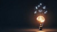 Glowing light bulb with business icons floating above representing innovation, creativity and entrepreneurial ideas on dark background.