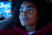 Young African American woman with natural curly hair gazing upward thoughtfully in evening blue light, wearing burgundy coat, close-up portrait showing genuine emotion.
