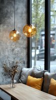 Modern cafe interior with amber glass pendant lights, concrete wall, wooden table, and yellow accent pillows against window view creating cozy atmosphere.