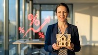 Businesswoman holding wooden house model with percentage and upward arrow symbols on glass window in modern office setting, representing real estate investment growth and property market success.