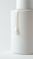 Creamy white cosmetic product dripping from cylindrical container on neutral background, isolated for skincare, beauty, and cosmetics marketing use.