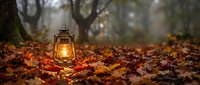 Vintage oil lantern glowing warmly among colorful autumn leaves in misty forest setting, creating cozy seasonal atmosphere for camping and outdoor adventures.