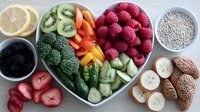 Fresh healthy ingredients arranged in heart shaped plate with berries, vegetables, fruits and chia seeds on white wooden background, top view composition.