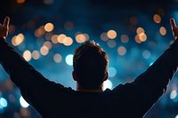 Silhouette of man with raised arms against blurred bokeh lights background in dark blue tones, expressing freedom, success and achievement.