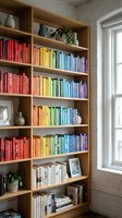 Modern home library with rainbow color-coded books organized on wooden shelves, bright reading nook with natural light for interior design inspiration.