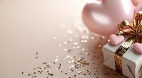 Pink balloons and wrapped gift box with golden ribbon on soft pink background with scattered glitter confetti for birthday party celebration.