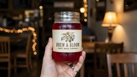 Hand holding a mason jar of homemade small batch kombucha in a cozy cafe with warm bokeh lights in the background.