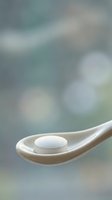 White pill tablet on wooden spoon with soft bokeh background for healthcare and medicine concepts.