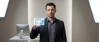 Male professional with dark hair and facial hair, appearing to be in his 30s of Caucasian ethnicity, wearing a dark blazer and shirt, holding a glowing digital envelope icon in a modern office setting for business communication concepts.