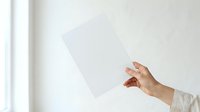 Female hand with manicured nails holding blank white card against neutral background, suitable for business presentations, greeting cards, and promotional materials.