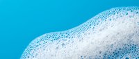 White foam bubbles on bright blue water surface creating abstract texture for spa wellness and cleaning product backgrounds.