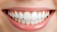 Close up view of healthy white teeth and natural pink lips showing bright confident smile against soft skin background. For dental and orthodontic advertising.