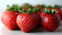 Fresh ripe strawberries with green leaves arranged in row on light background, macro shot showing detailed texture and natural juicy appearance.