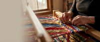 Traditional carpet weaving artisan working on colorful handmade rug with intricate patterns in workshop setting showcasing cultural craftsmanship and textile art.