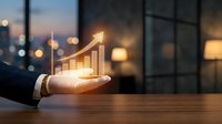 Businessman hand holding glowing upward arrow chart above wooden table with blurred city skyline at dusk, representing financial growth, success, and business development strategy.
