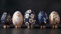 Luxury decorative Easter eggs with floral patterns in navy blue and gold on dark background. Elegant porcelain collectibles on golden stands.