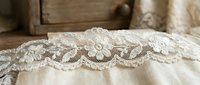 Delicate white lace trim with ornate scalloped edges on cream fabric, perfect for wedding dress embellishment, bridal wear design, textile decoration, and vintage fashion projects.
