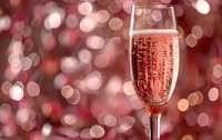 Glass of rose sparkling wine with bubbles against blurred festive red and pink bokeh background, romantic celebration atmosphere.