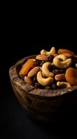 Mixed nuts and dried fruits in rustic wooden bowl on dark background for healthy snacking and gourmet food photography.