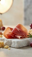 Sliced prosciutto ham on marble board with cheese, olives and rosemary for gourmet appetizer platter and charcuterie board presentation.