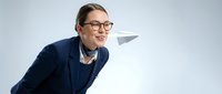 Young Caucasian male professional wearing glasses and navy blazer throws paper airplane, symbolizing innovation, startup ideas, and business strategy on white background.