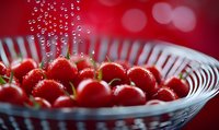 Fresh cherry tomatoes with water drops in glass bowl against red background, selective focus creates dreamy bokeh effect, macro food photography.