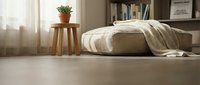 Cozy bedroom interior with unmade bed, wooden stool, potted plant and bookshelf creating warm minimalist home decor atmosphere for relaxation.