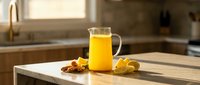 Fresh orange juice in glass pitcher on wooden cutting board with orange slices and almonds in modern kitchen setting for healthy breakfast concept.