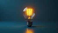 Glowing vintage incandescent bulb with warm yellow filament on dark blue background, symbolizing innovation, creativity, ideas and energy solutions for business and technology concepts.