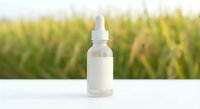 White dropper bottle with pipette on clean surface against blurred natural green field background for skincare cosmetics and wellness products.