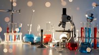 Laboratory equipment with microscope and colorful chemical solutions in glass beakers and test tubes for scientific research and experimentation.