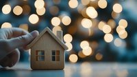 Hand holding small wooden house model with warm bokeh lights creating cozy atmosphere for real estate and home ownership concepts.