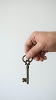 Hand holding vintage brass key against white background for real estate, security, and access concepts.