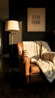 Cozy living room corner with leather armchair, faux fur blanket, ceramic mug, floor lamp, and stay home wall art in warm light.